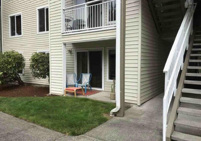 Ground-level patio with two blue chairs and a small table, next to a staircase and sliding glass doors on a Parkview Mukilteo Condo apartment building.