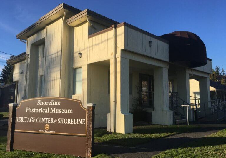 A beige building labeled Shoreline Historical Museum Heritage Center at Shoreline stands under a clear blue sky, with a sign in front and a ramp leading to the entrance, inviting visitors to explore Shoreline history at this local museum.