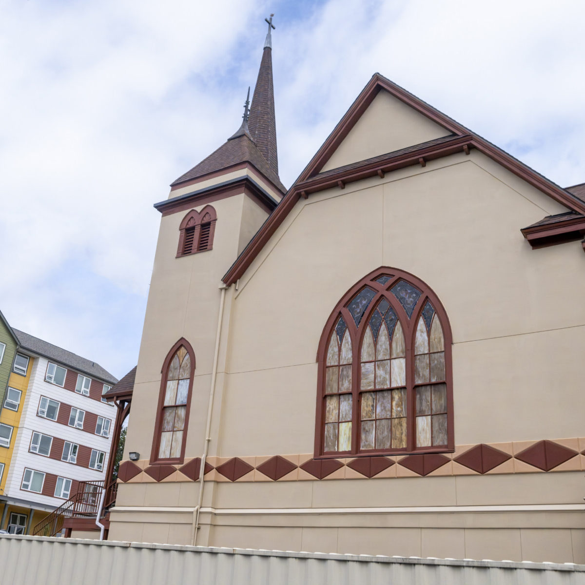 A beige church with stained glass windows and a tall steeple stands next to a green apartment building under a cloudy sky, reflecting the architectural diversity found in neighborhoods shaped by Washington Community Reinvestment Association history.