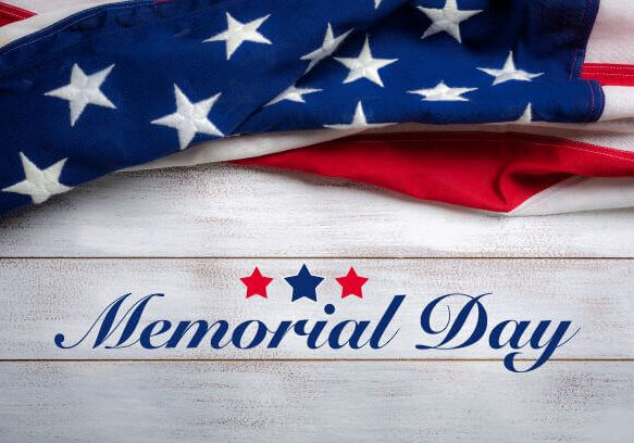 A folded American flag rests above the words “Memorial Day” written in blue script on a white wooden background with three stars, creating a heartfelt tribute to Memorial Day.